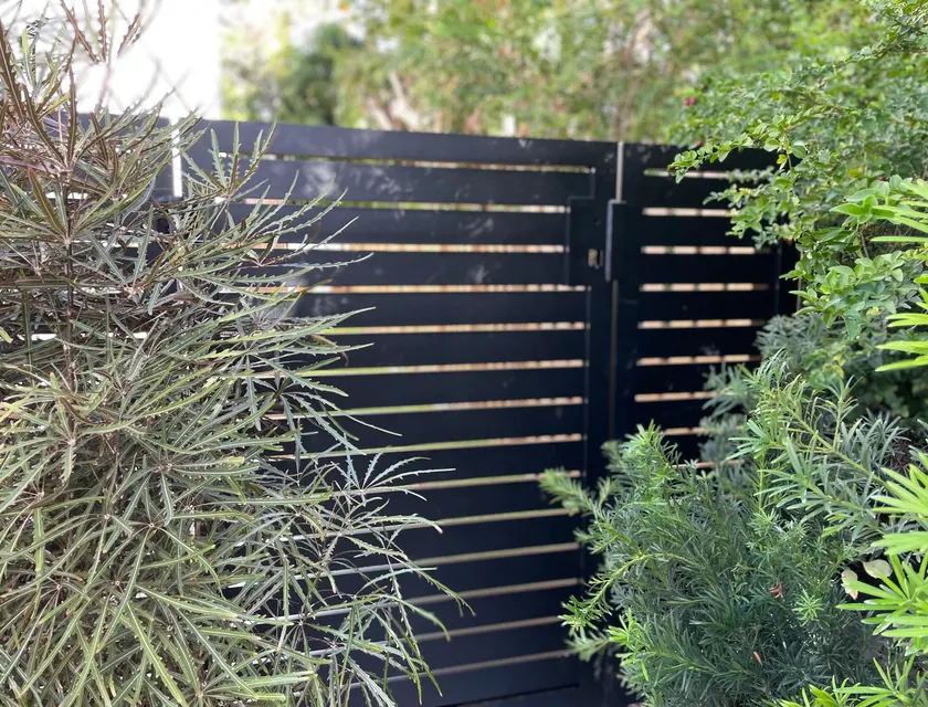 Matte black custom horizontal slat aluminum walk gate in tropical landscape with narrow slat spacing