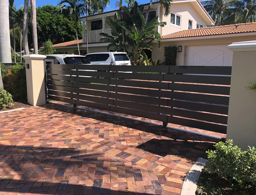 Charcoal powder coated horizontal aluminum slide gate spanning a brick paver driveway with keypad access